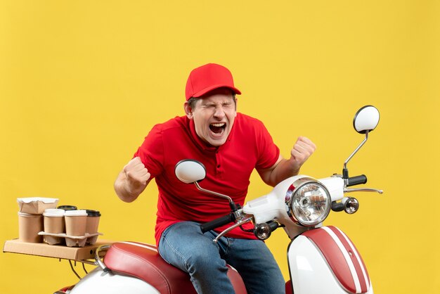 Vista frontale del giovane ragazzo nervoso che indossa la camicetta rossa e il cappello che trasporta gli ordini su priorità bassa gialla