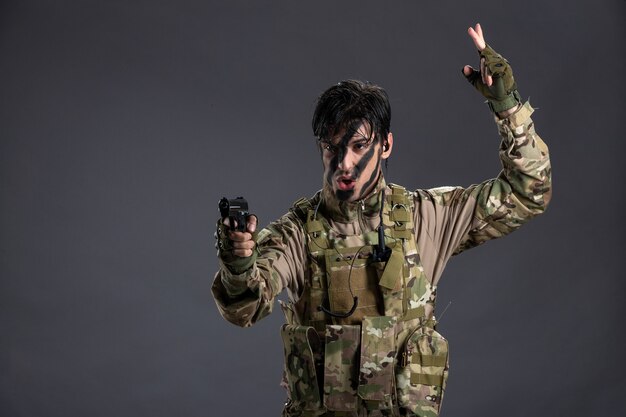 Vista frontale del giovane soldato in mimetica che punta la pistola sul muro scuro