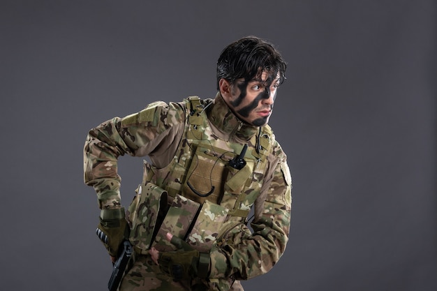 Vista frontale del giovane soldato in mimetica con la pistola sul muro scuro