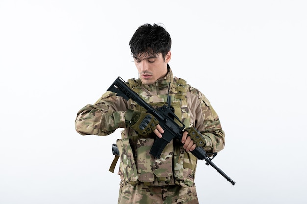 Vista frontale del giovane soldato in mimetica con mitragliatrice muro bianco