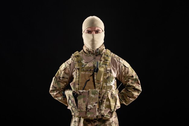 Vista frontale del giovane soldato in uniforme e maschera sul muro nero