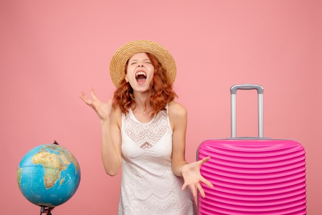 Vista frontale del giovane turista femminile con borsa rosa che grida sulla parete rosa