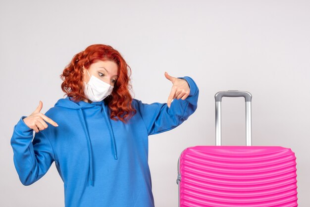 Vista frontale del giovane turista femminile con borsa rosa in maschera sul muro bianco