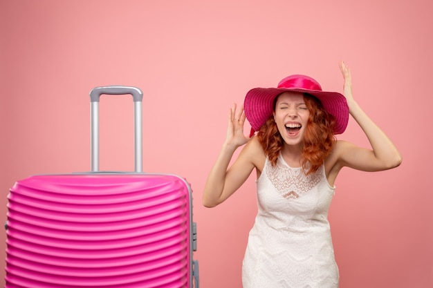 Vista frontale del giovane turista femminile con cappello rosa e borsa che si rallegra sulla parete rosa
