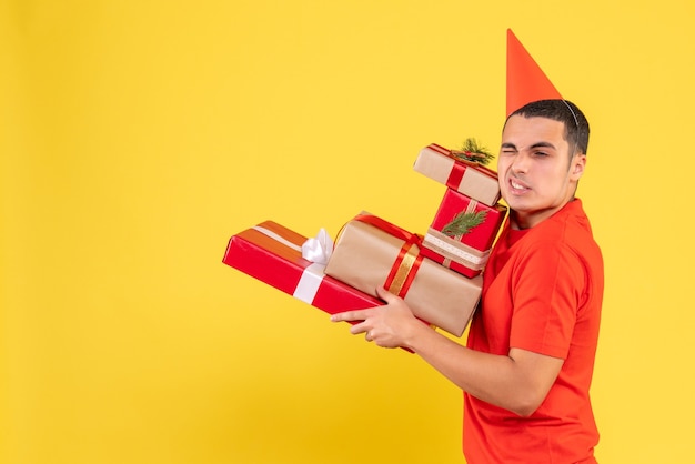 Vista frontale del giovane uomo che porta i regali di Natale sulla parete gialla