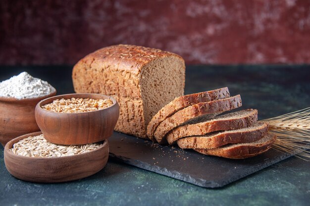 Vista frontale del grano saraceno della farina d'avena della farina delle fette del pane nero sul bordo di colore scuro su fondo afflitto blu