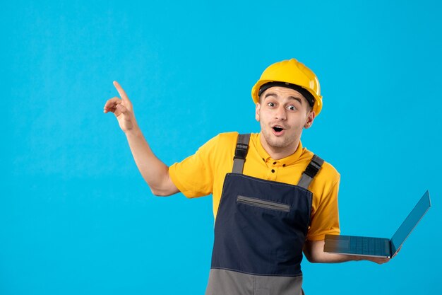 Vista frontale del lavoratore maschio eccitato in uniforme con il computer portatile sulla superficie blu