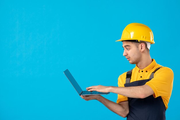 Vista frontale del lavoratore maschio in uniforme che lavora con il computer portatile sull'azzurro