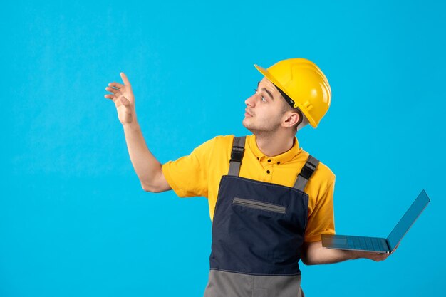 Vista frontale del lavoratore maschio in uniforme con il computer portatile che osserva da parte sull'azzurro