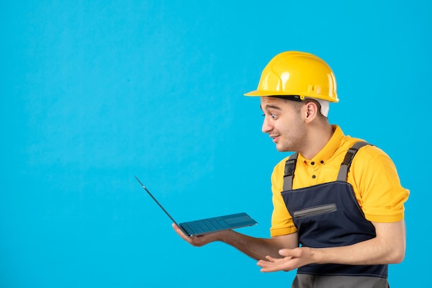 Vista frontale del lavoratore maschio in uniforme con il computer portatile sull'azzurro