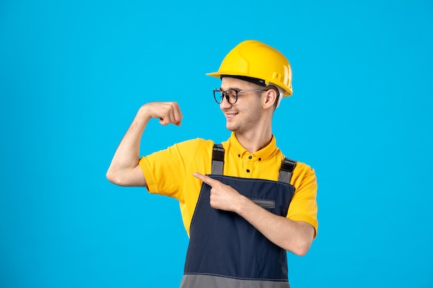 Vista frontale del lavoratore maschio in uniforme gialla che sorride e che flette sull'azzurro