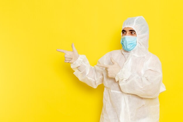 Vista frontale del lavoratore scientifico maschio in abito bianco protettivo speciale con maschera sulla parete giallo chiaro