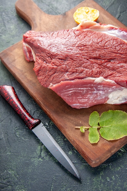 Vista frontale del limone crudo fresco delle carni rosse sul tagliere e sul coltello di legno marroni sul fondo di colore scuro