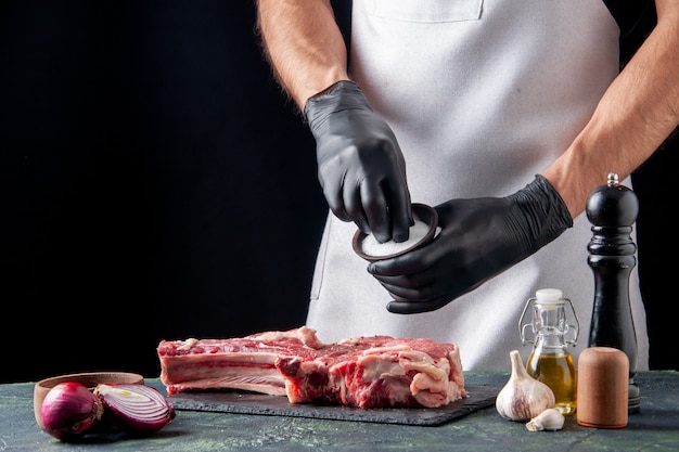 Vista frontale del macellaio maschio che sala la carne su una superficie scura