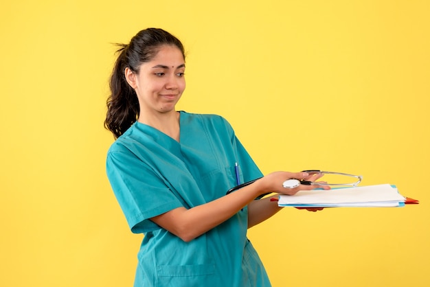 Vista frontale del medico della donna in uniforme che dà i documenti sulla parete gialla