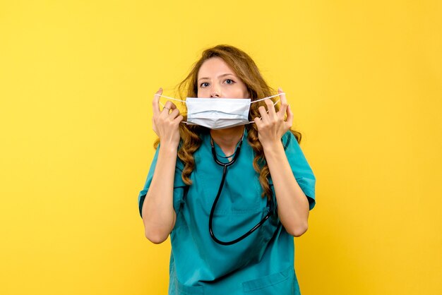 Vista frontale del medico femminile che indossa la maschera sulla parete gialla