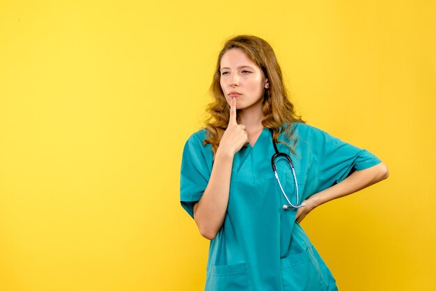 Vista frontale del medico femminile che pensa sulla parete gialla