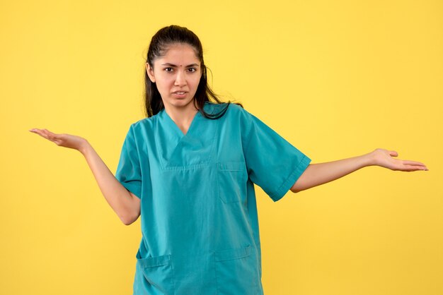 Vista frontale del medico femminile grazioso che apre le sue mani sulla parete gialla