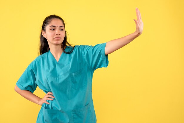 Vista frontale del medico femminile grazioso che ferma qualcosa sulla parete gialla