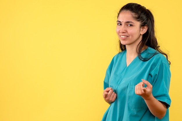 Vista frontale del medico femminile grazioso che indica nella parte anteriore sulla parete gialla