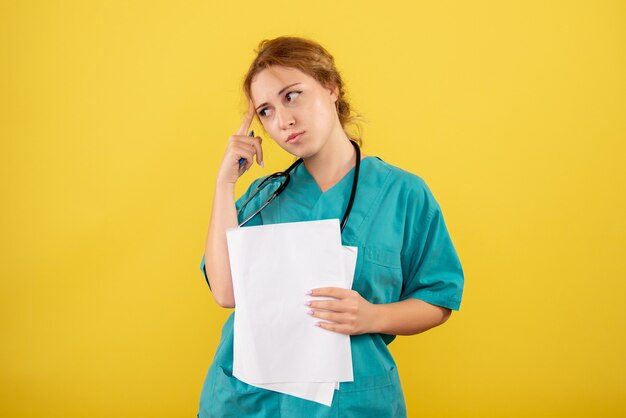 Vista frontale del medico femminile in tuta medica che tiene analisi sulla parete gialla