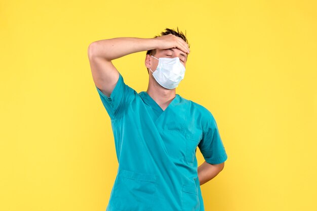 Vista frontale del medico maschio che ha mal di testa sulla parete gialla