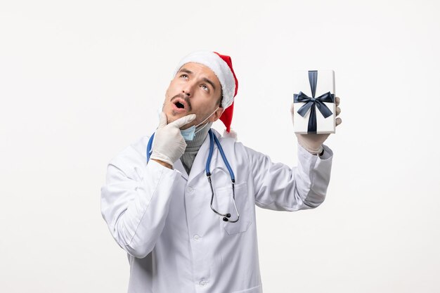 Vista frontale del medico maschio che tiene presente sul muro bianco