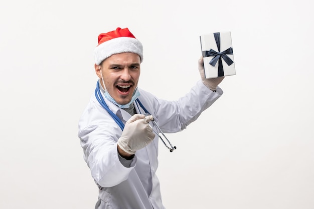 Vista frontale del medico maschio che tiene presente sul muro bianco