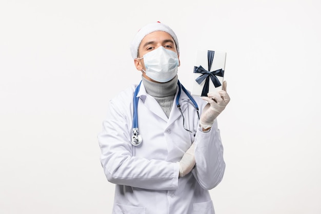 Vista frontale del medico maschio che tiene presente sul muro bianco