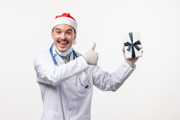 Vista frontale del medico maschio che tiene presente sul muro bianco