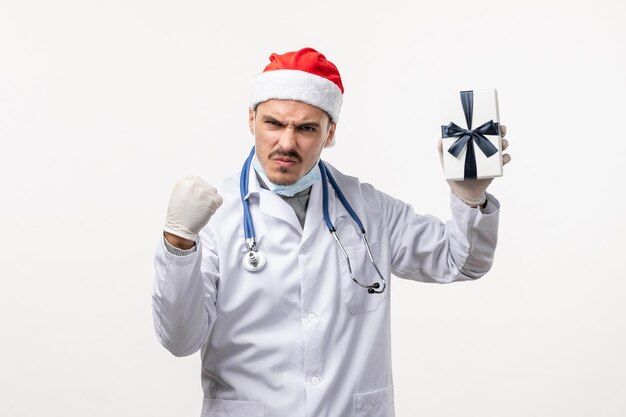 Vista frontale del medico maschio che tiene presente sul muro bianco