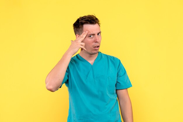 Vista frontale del medico maschio con espressione di pensiero sulla parete gialla