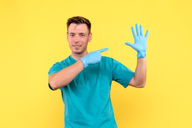 Vista frontale del medico maschio con guanti blu su emozione medica ospedale pavimento giallo