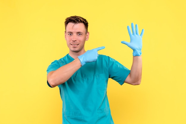 Vista frontale del medico maschio con guanti blu su emozione medica ospedale pavimento giallo