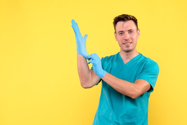 Vista frontale del medico maschio con guanti blu sulla parete gialla