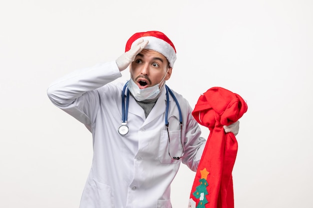 Vista frontale del medico maschio con la borsa regalo rossa sul muro bianco