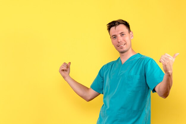 Vista frontale del medico maschio con la faccia sorridente sulla parete gialla