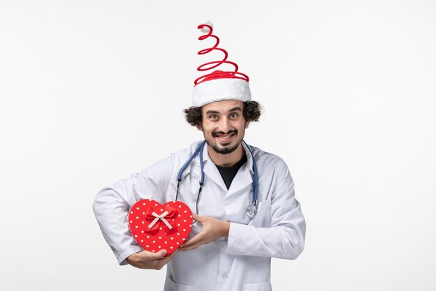 Vista frontale del medico maschio con regalo di festa sul muro bianco