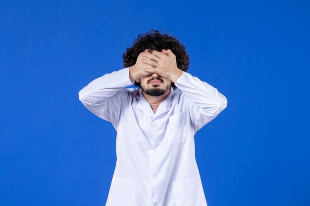 Vista frontale del medico maschio deluso in tuta medica su sfondo blu medicina ospedaliera farmaco covid- virus pandemia salute coronavirus vaccino