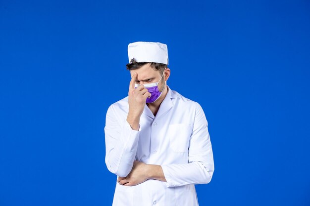 Vista frontale del medico maschio di pensiero in vestito medico e maschera viola sull'azzurro