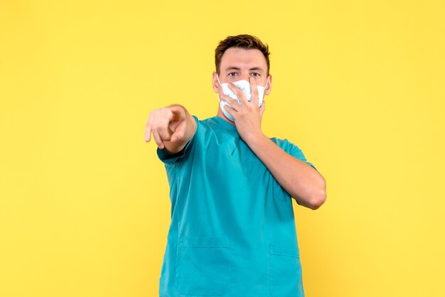 Vista frontale del medico maschio in maschera sterile sul pavimento giallo pandemia virus covid- medic