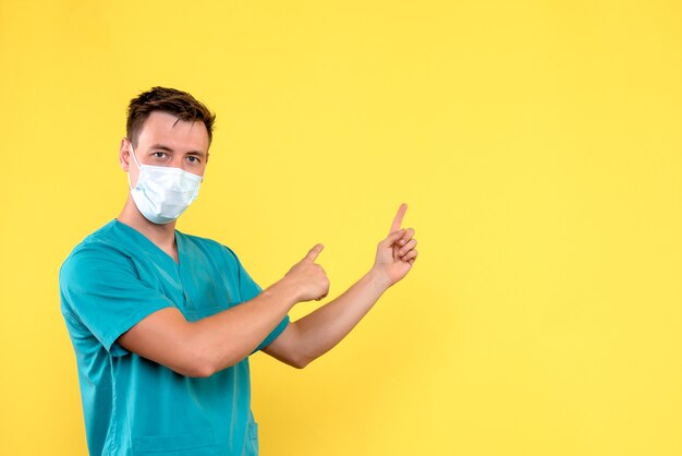 Vista frontale del medico maschio in maschera sul muro giallo chiaro