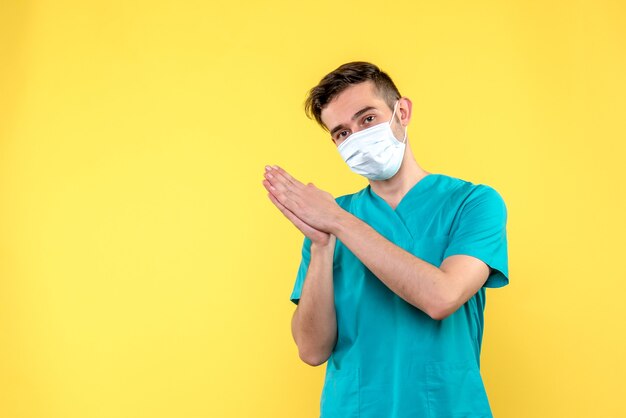 Vista frontale del medico maschio in maschera sulla parete gialla