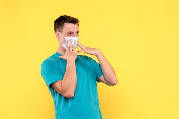 Vista frontale del medico maschio in maschera sulla parete gialla