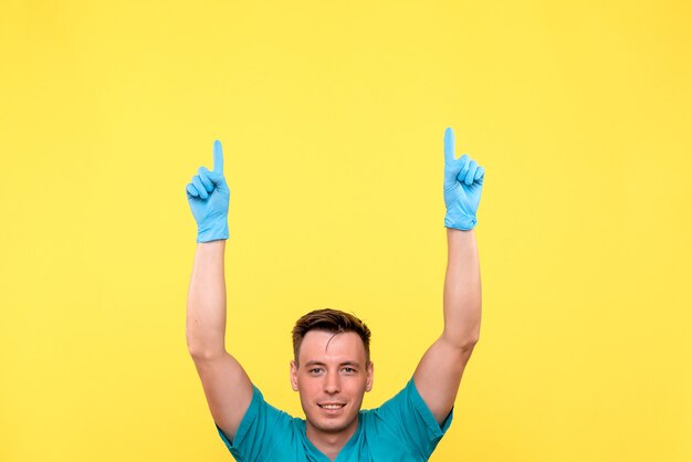 Vista frontale del medico maschio in posa con guanti blu sulla parete gialla
