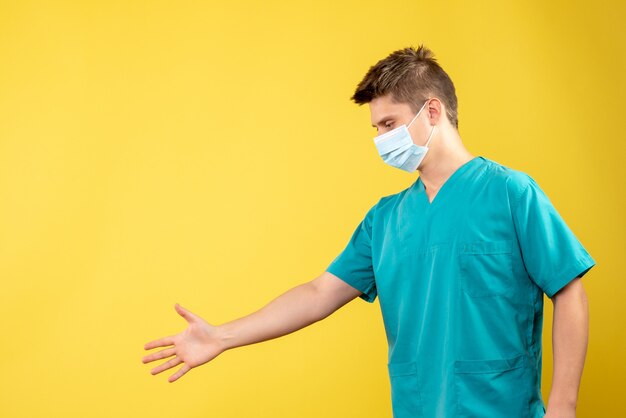 Vista frontale del medico maschio in tuta medica con maschera sterile che agitano le mani sulla parete gialla