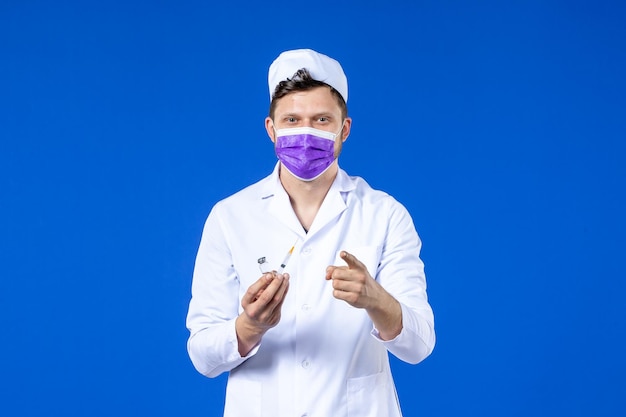 Vista frontale del medico maschio in tuta medica e maschera con iniezione e vaccino sull'azzurro