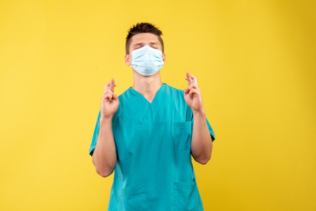 Vista frontale del medico maschio in tuta medica e maschera sterile sperando sulla parete gialla