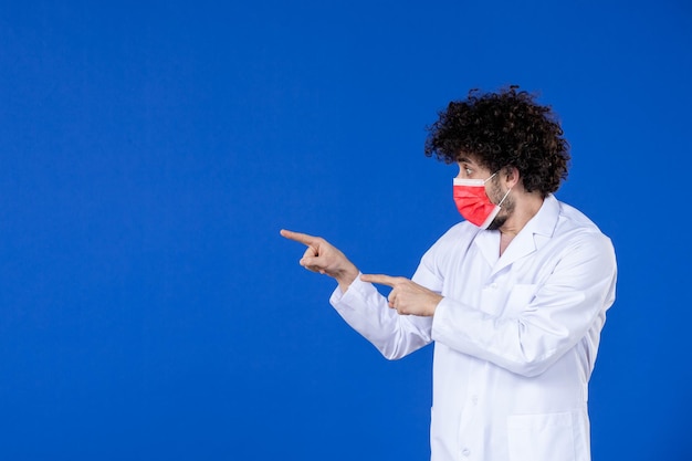 Vista frontale del medico maschio in tuta medica e maschera su sfondo blu vaccino ospedale covid- virus salute pandemia coronavirus farmaco