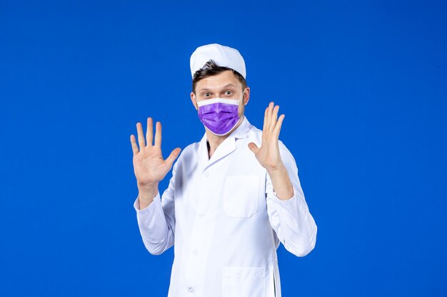 Vista frontale del medico maschio in tuta medica e maschera viola sull'azzurro